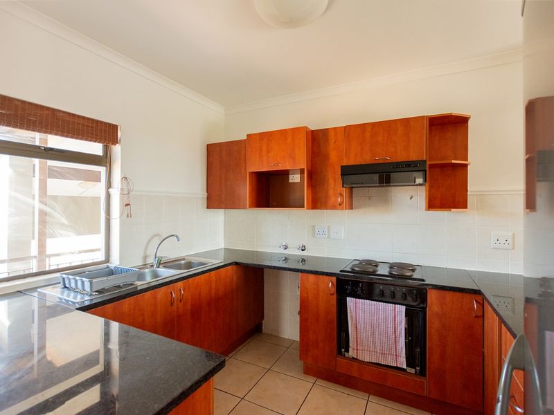 A functional kitchen featuring wooden cabinetry, granite countertops, a built-in oven with electric hob, and a tiled backsplash.