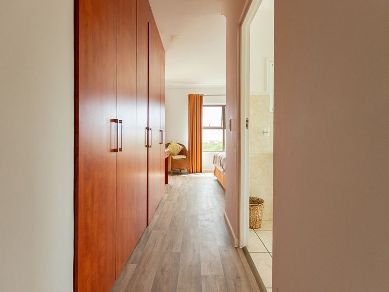A hallway featuring built-in wooden cupboards and laminate flooring, providing access to a bedroom and an adjacent bathroom.