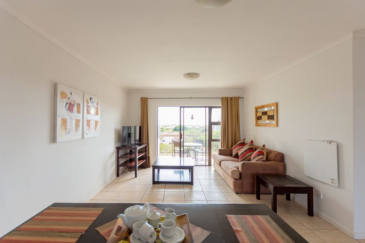 A bright living room featuring tiled flooring, a wall-mounted heater, and a sliding glass door providing access to an outdoor balcony area.