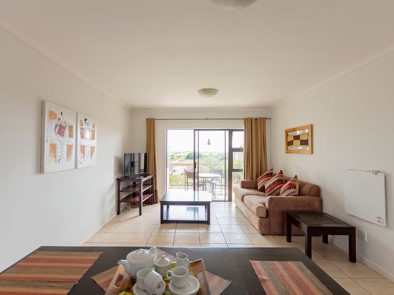 A bright living room featuring tiled flooring, a wall-mounted heater, and a sliding glass door providing access to an outdoor balcony area.