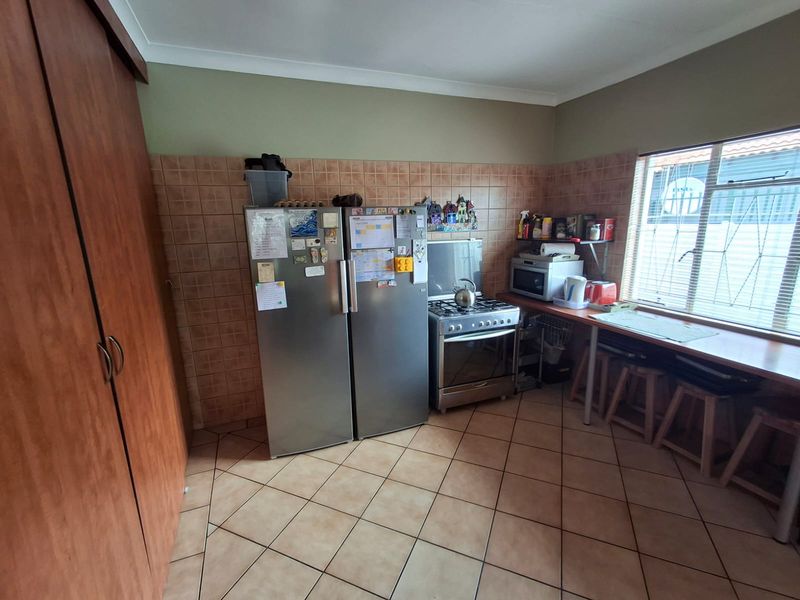 A functional kitchen featuring tiled flooring, a tiled splashback, built-in cabinetry, and a freestanding stove with a window providing natural light.
