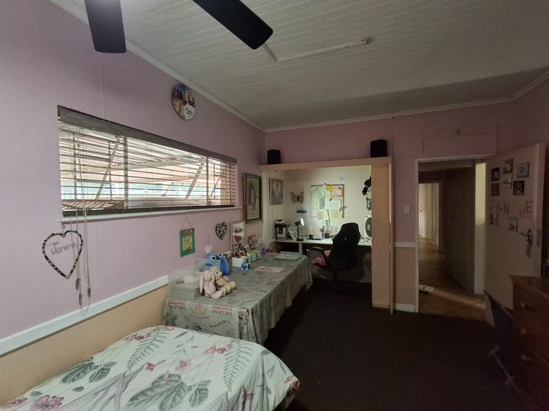 A bedroom featuring a built-in desk area, ceiling fan, and horizontal blinds, with a dated interior finish.
