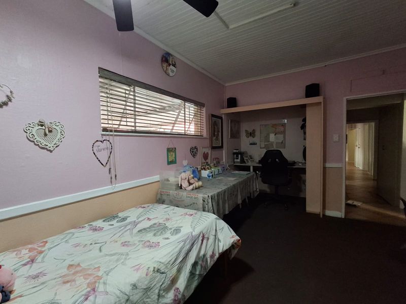 A bedroom featuring a built-in desk area, tongue and groove ceiling, and a ceiling fan, offering a functional space with potential for modernization.