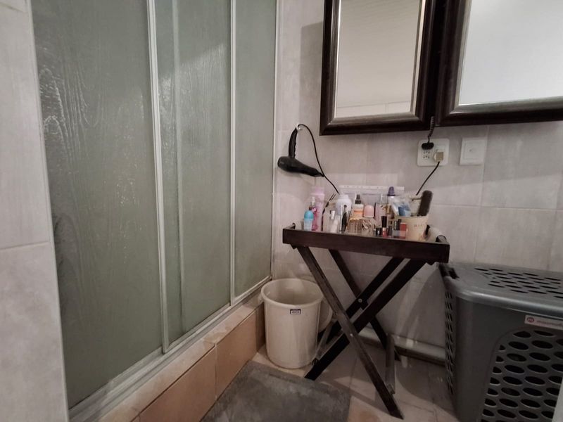 A functional bathroom featuring a shower enclosure with sliding doors and wall-mounted mirror, requiring some maintenance to the tiled finishes.