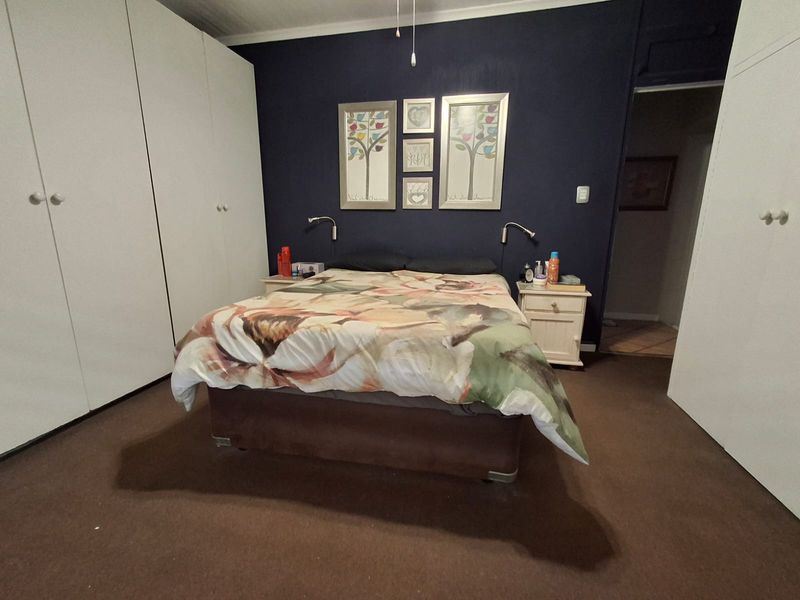 A bedroom featuring dark blue accent wall, extensive white built-in cupboards, and wall-mounted reading lights.