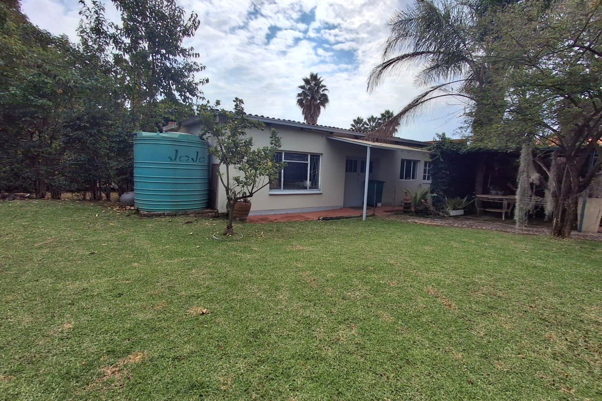 Rear view of the property featuring a spacious lawn, established garden, covered patio area, and a large water storage tank.