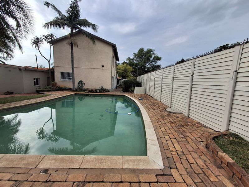Outdoor pool area featuring a swimming pool, brick paved surround, and high perimeter fencing with security spikes.