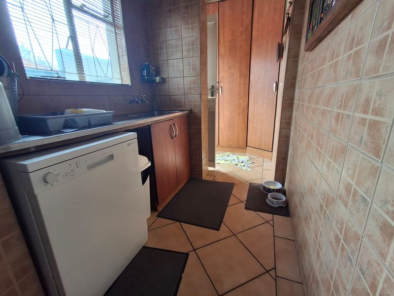 A functional laundry room featuring tiled walls and flooring, built-in cabinetry, and a stainless steel sink with plumbing connections.