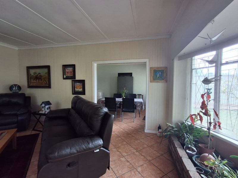 A living room featuring tiled flooring and a large bay window with security bars, leading into an adjacent dining area.