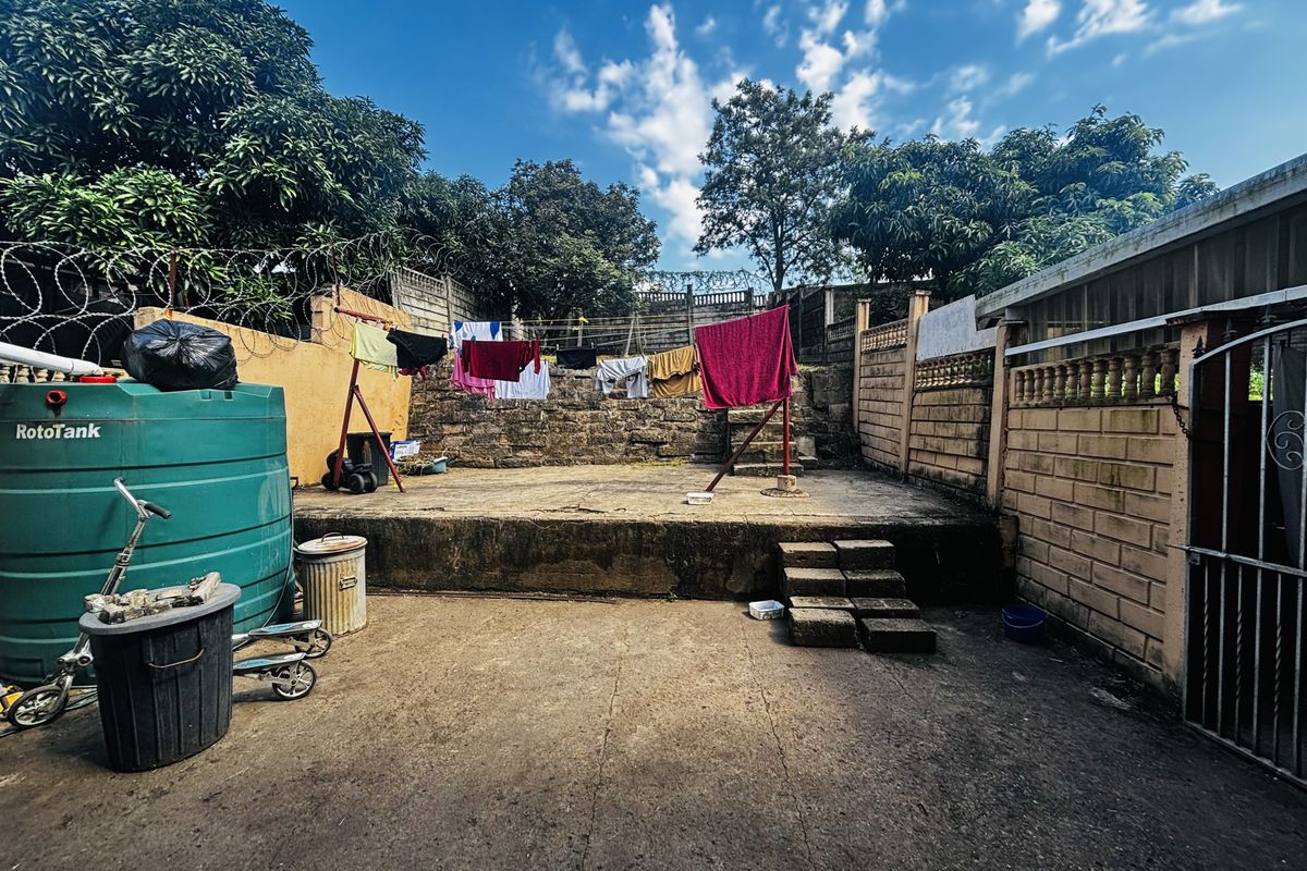 Rear exterior area featuring a concrete patio, retaining wall, and water storage tank, enclosed by a perimeter wall with security fencing.