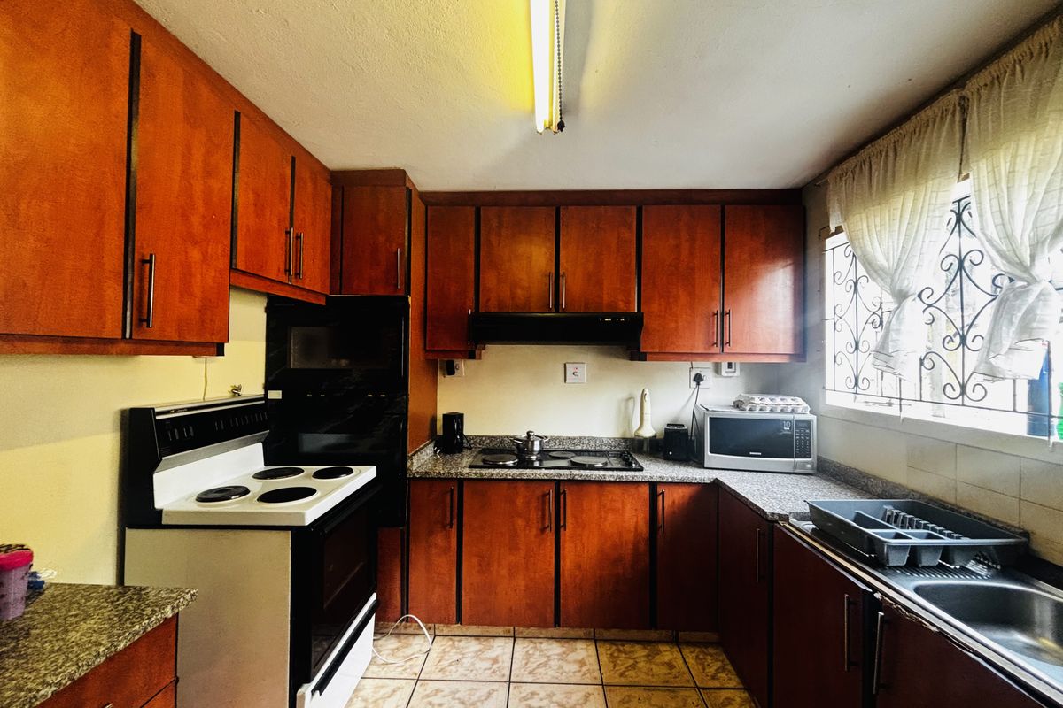 A functional kitchen featuring wood-finish cabinetry, granite countertops, an electric stove, and a double sink with security bars on the window.