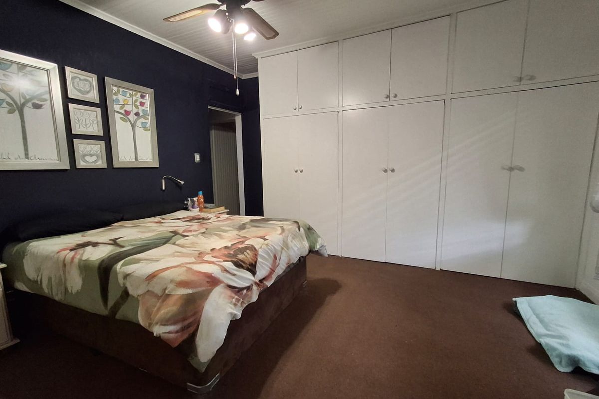 Spacious bedroom featuring extensive floor-to-ceiling built-in cupboards, a ceiling fan, and dark blue accent wall.