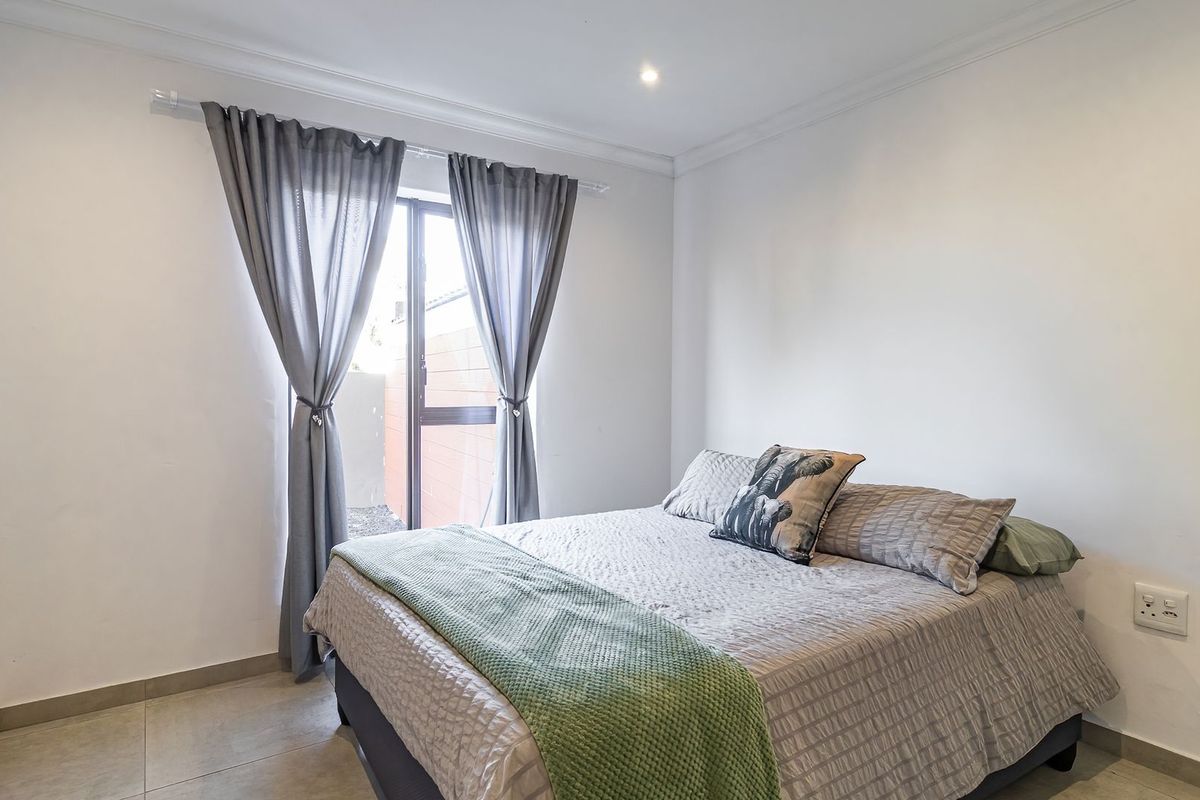 A bright bedroom featuring tiled flooring, neutral walls, and a sliding glass door providing access to the exterior.