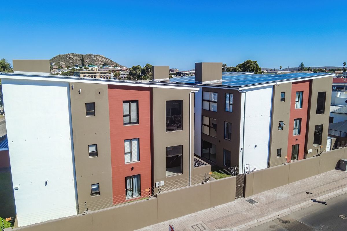 Aerial view of a modern multi-story apartment complex featuring solar panels on the roof and secure perimeter walling.