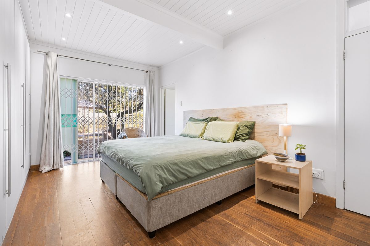 Bright bedroom featuring timber flooring, a tongue and groove ceiling with recessed lighting, and a sliding glass door providing access to the exterior.