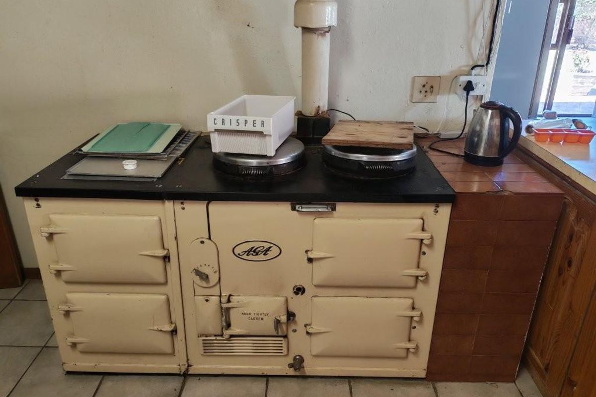 A classic cream-colored AGA range cooker installed in a kitchen with tiled flooring and a tiled side counter.