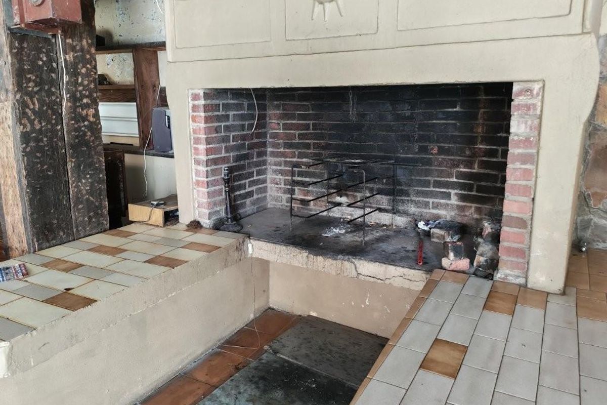 A rustic indoor braai or fireplace area featuring a brick hearth, tiled prep surfaces, and a large masonry chimney breast.