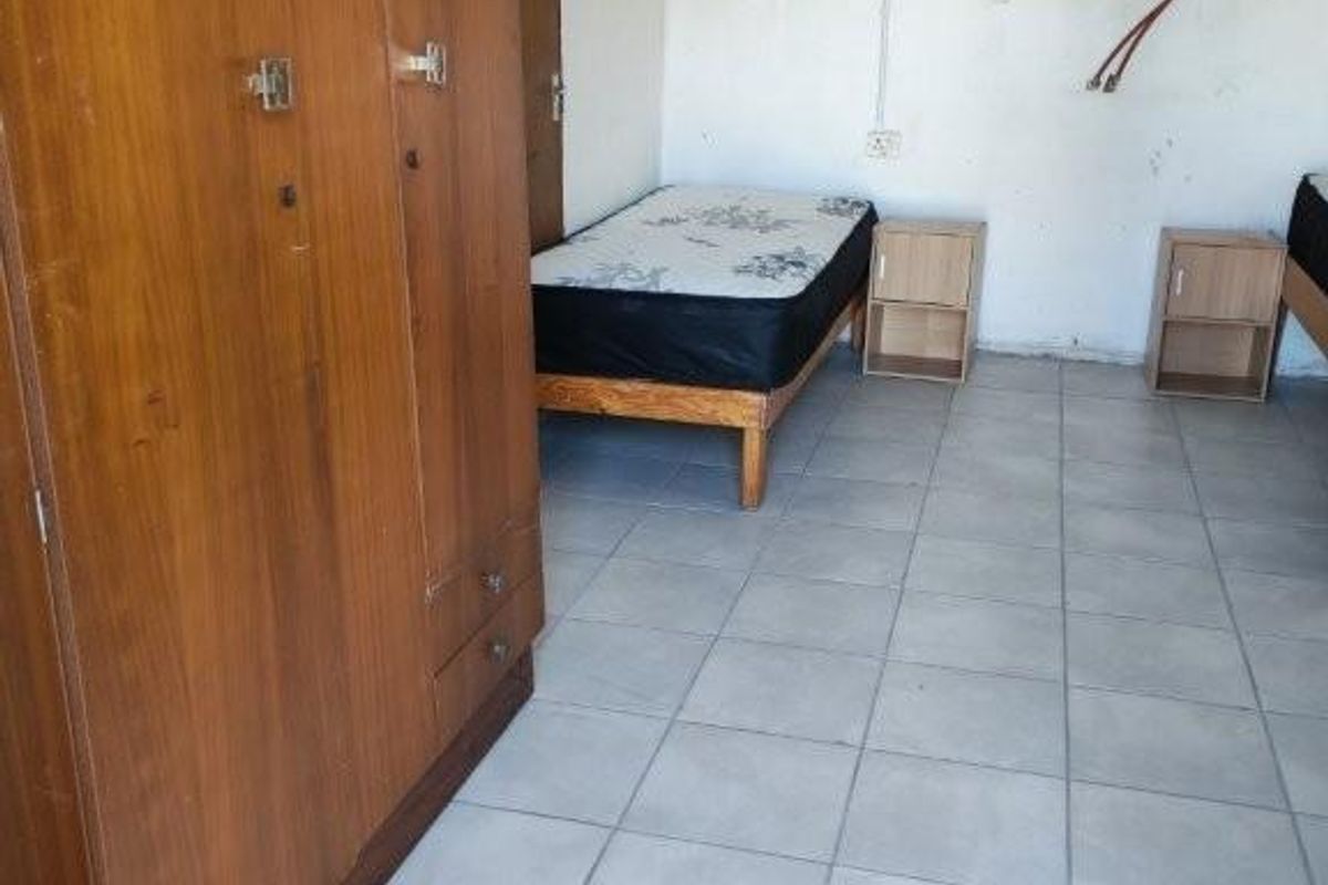 A bedroom featuring tiled flooring and a security-grilled window, currently showing signs of wear and exposed electrical wiring.