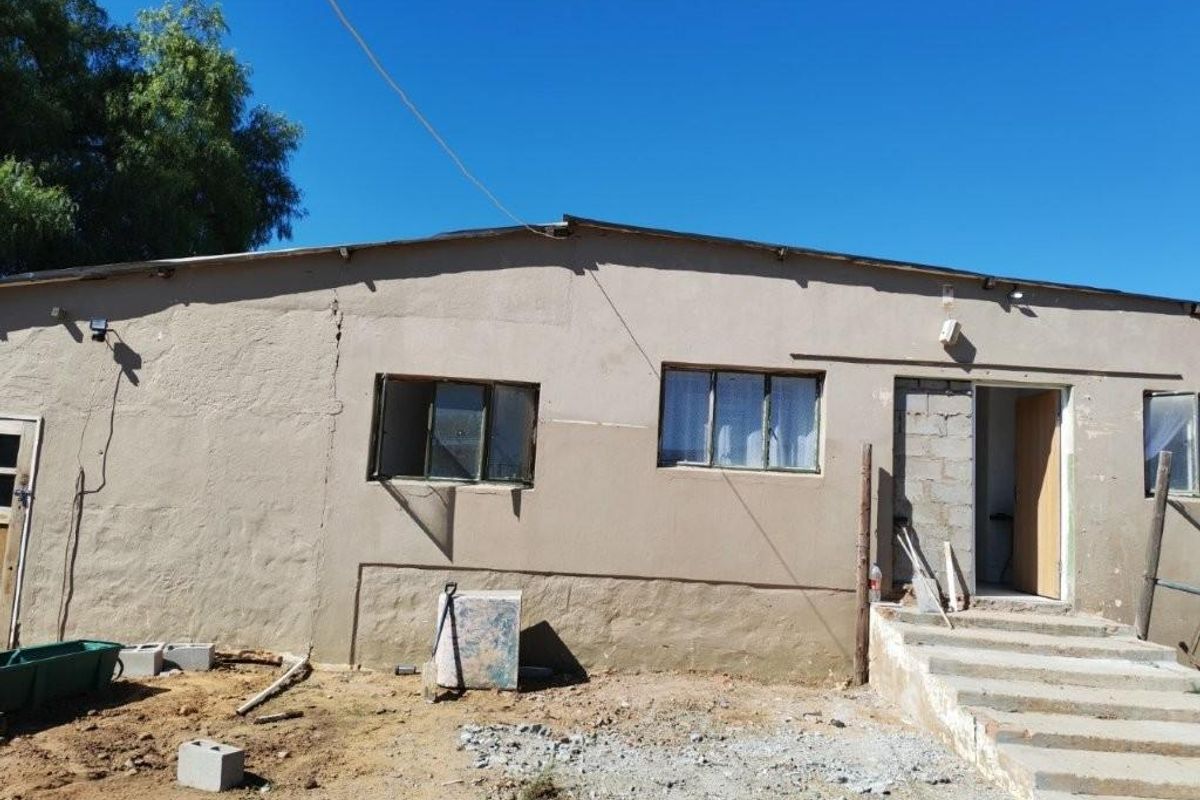Exterior view of a small holding dwelling showing unfinished plasterwork, exposed masonry around the entrance, and concrete steps requiring maintenance.