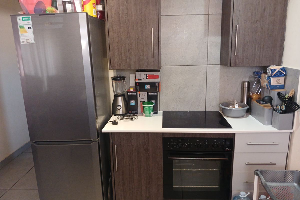 Compact kitchen area featuring dark wood-look cabinetry, a built-in oven, electric hob, and tiled splashback.
