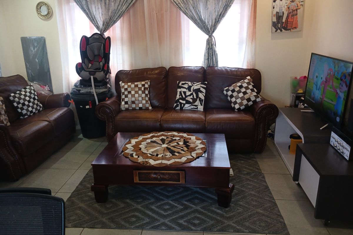 A comfortable living room featuring tiled flooring and large windows with curtains, providing a functional space for relaxation and entertainment.