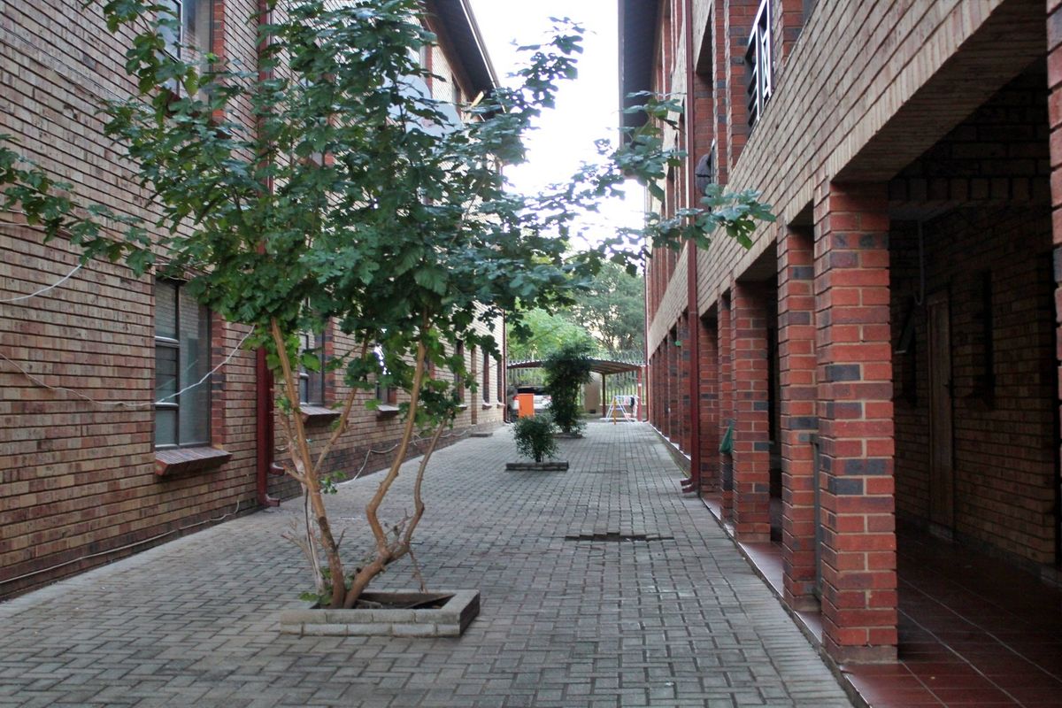 A view of the paved exterior walkway between apartment blocks, featuring face brick construction and covered access areas.