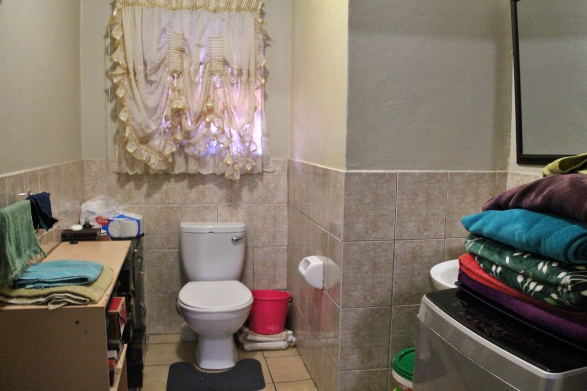 A functional bathroom featuring ceramic wall and floor tiling, a standard toilet, and a washbasin, providing essential utility space.