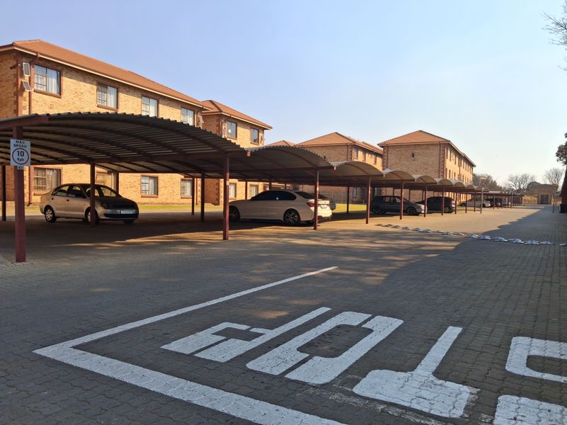 Exterior view of the apartment complex featuring covered parking bays and a paved driveway area.