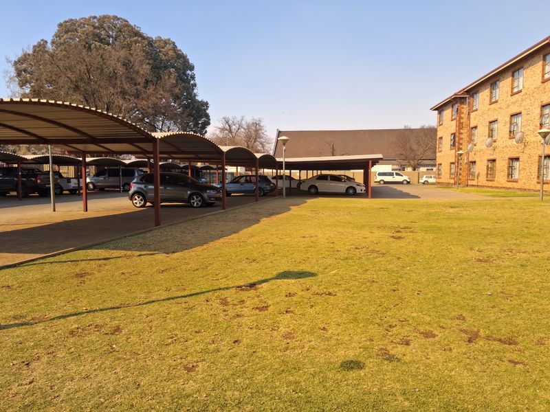 Exterior view of the apartment complex featuring a large lawn area and covered parking bays for residents.