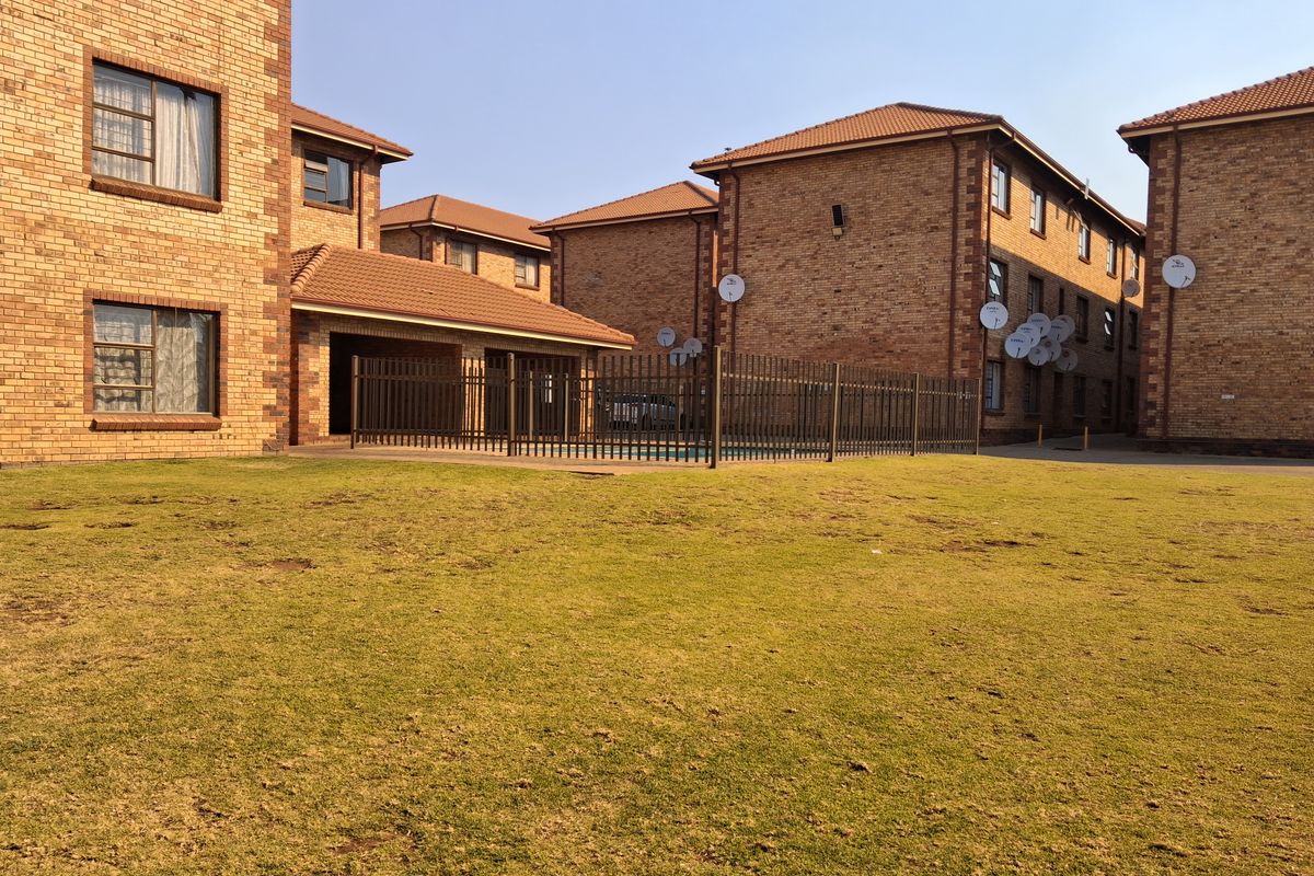 Exterior view of a residential apartment complex featuring face brick buildings, a communal swimming pool area, and landscaped lawn.