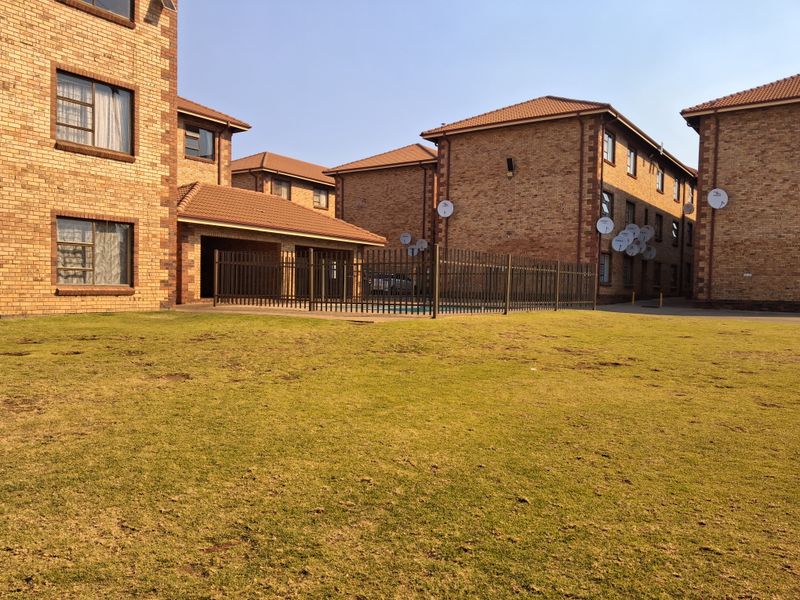Exterior view of a residential apartment complex featuring face brick buildings, a communal swimming pool area, and landscaped lawn.