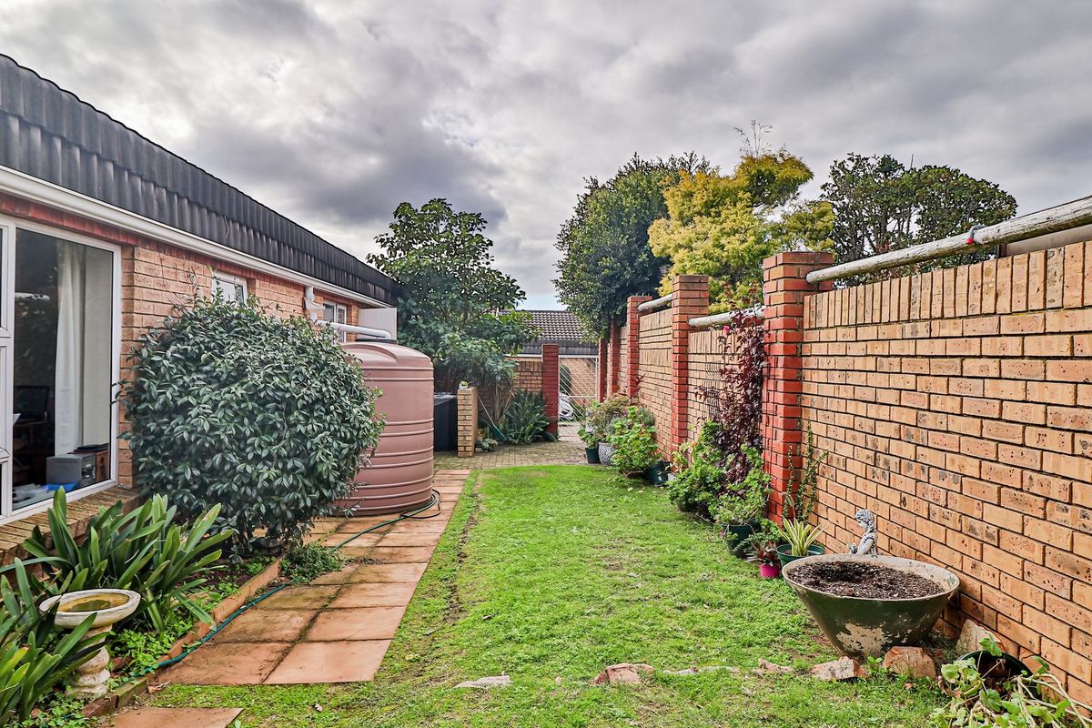A private rear garden featuring a brick boundary wall, paved walkway, and a water storage tank alongside the townhouse exterior.