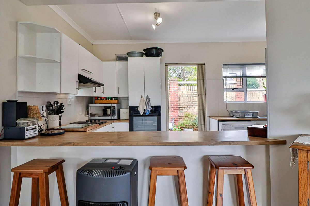 A functional kitchen featuring white cabinetry, a wooden breakfast bar, built-in oven, and extractor fan, with direct access to the rear outdoor area.