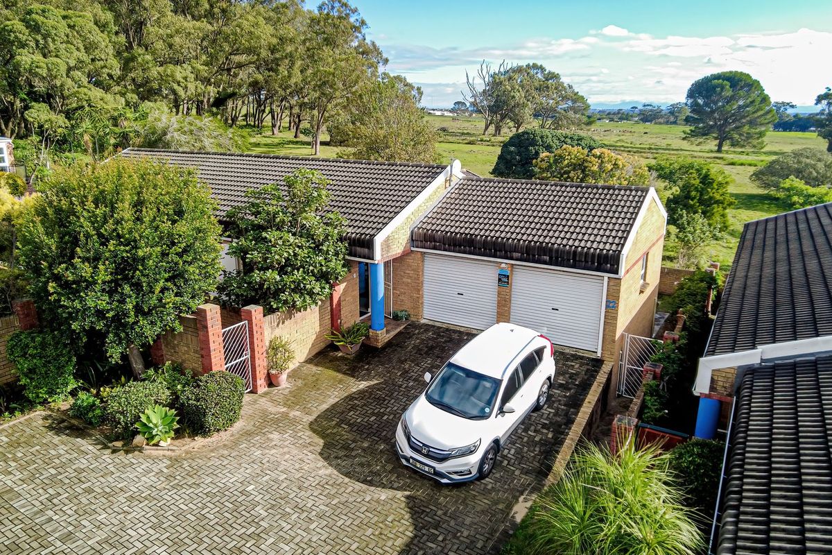 Aerial view of a townhouse featuring a double garage, paved driveway, and brick facade, set against a scenic rural landscape.