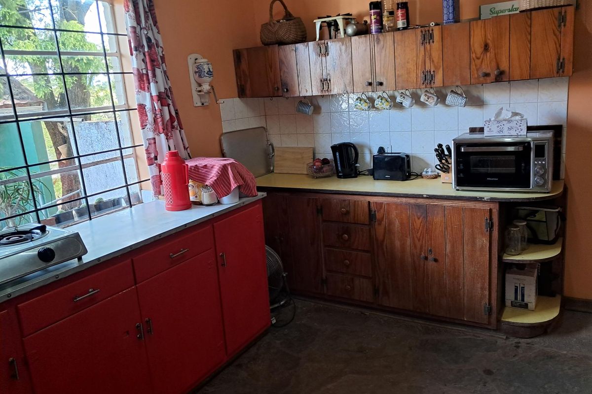 A functional kitchen featuring a mix of wooden and red cabinetry, tiled backsplash, and ample counter space with a large window for natural light.