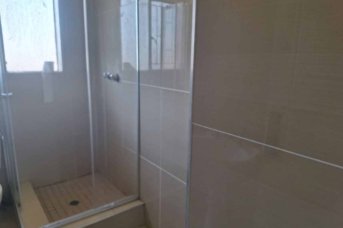 A functional bathroom featuring a glass-enclosed shower with neutral wall tiling and a raised shower base.