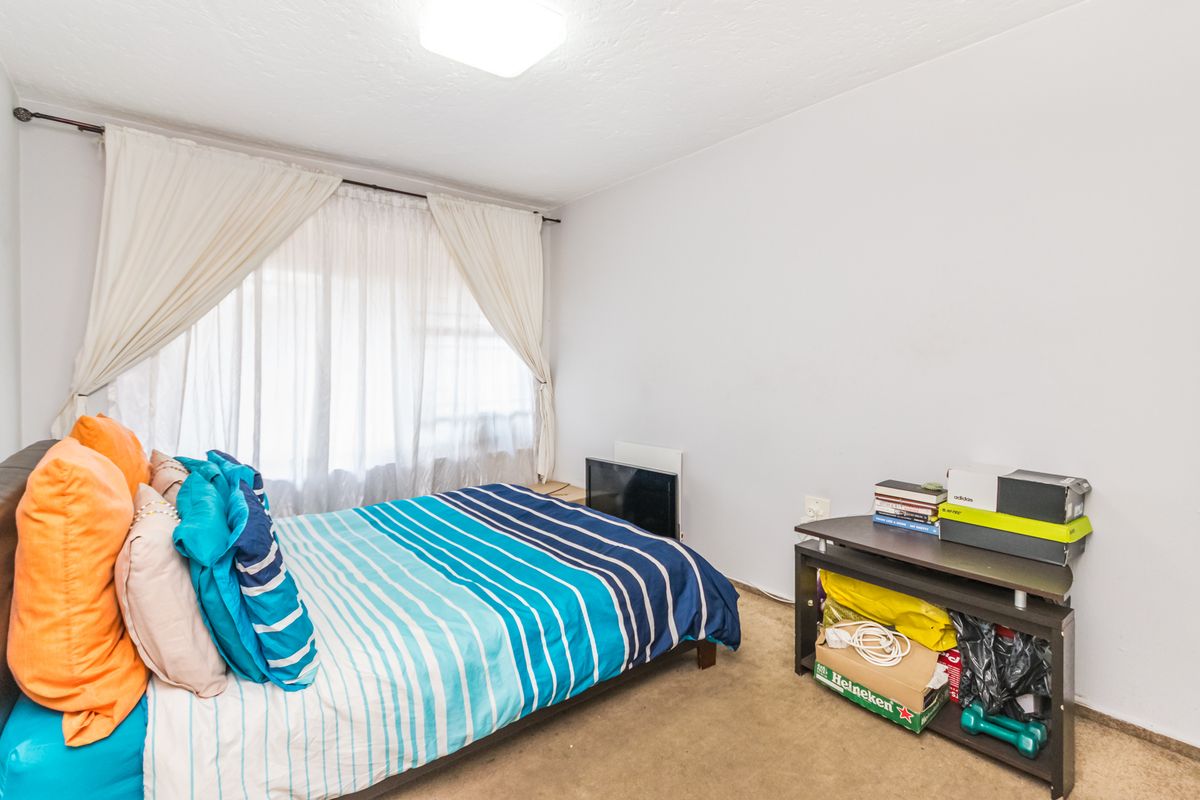 A standard bedroom featuring neutral walls, carpeted flooring, and a large window with installed curtain rods.
