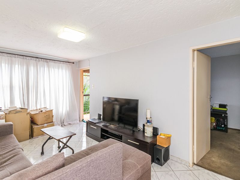 A living room area featuring tiled flooring and access to an adjacent room, currently used as a living space.
