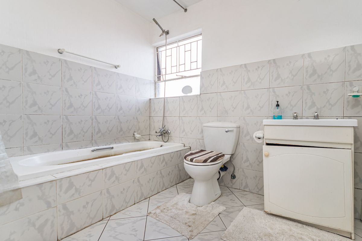 A functional bathroom featuring a bathtub, toilet, and vanity basin with tiled finishes and security bars on the window.