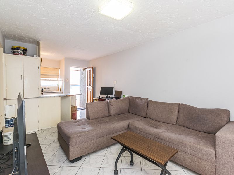 Open-plan living area featuring tiled flooring and built-in kitchen cabinetry, providing a functional layout with direct access to the exterior entrance.