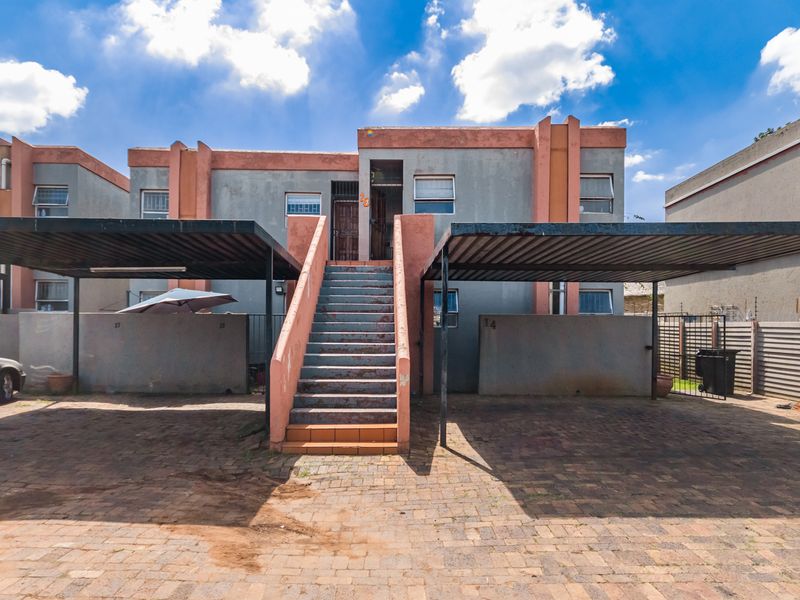 Front exterior view of an apartment complex featuring a paved driveway, covered carports, and a central external staircase leading to the upper level.