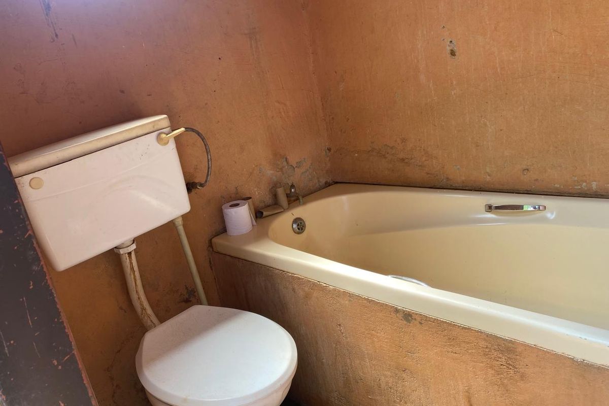 A dated bathroom featuring a standard bathtub and toilet, requiring significant renovation and wall surface repairs to restore functionality and aesthetic appeal.