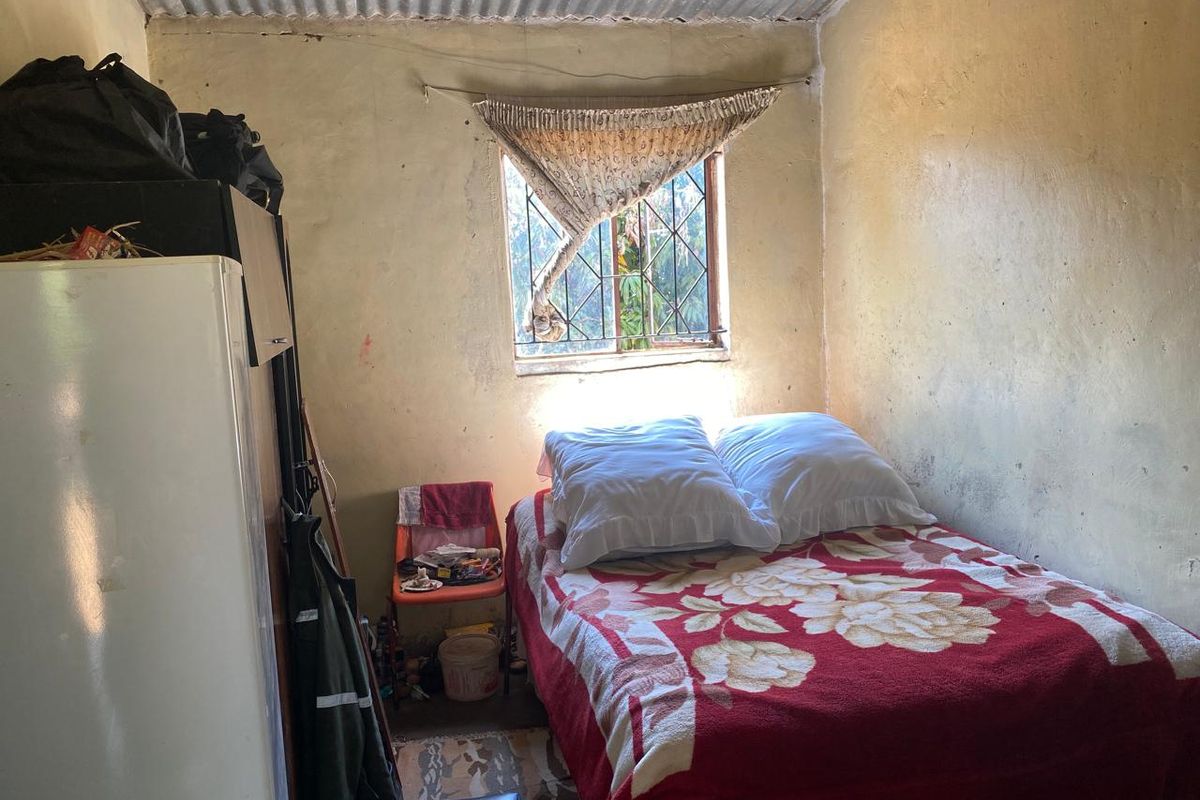 A compact bedroom featuring a corrugated metal ceiling and a window with security bars, requiring significant cosmetic updates to improve the living space.