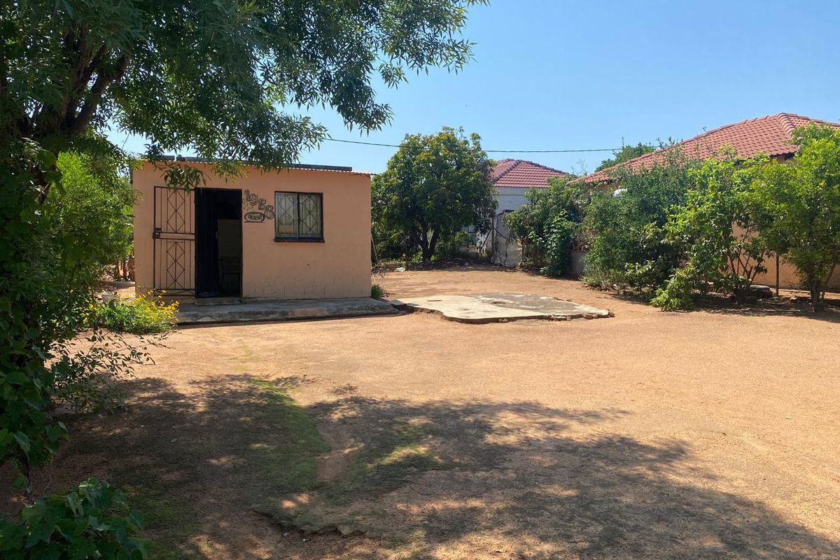 Rear yard area featuring a detached outbuilding with security gate and bars, alongside a concrete slab and mature garden landscaping.