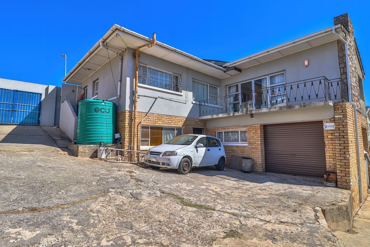 Rear exterior view of a multi-level house featuring a concrete driveway, roller garage door, balcony, and an external water storage tank.
