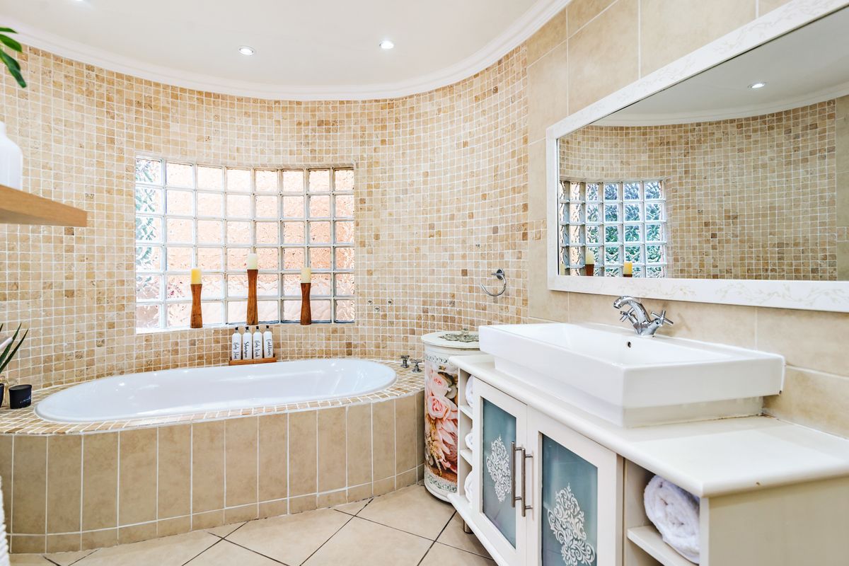 A well-maintained bathroom featuring a built-in bathtub, a vanity with a vessel sink, mosaic wall tiling, and a distinctive glass block window.