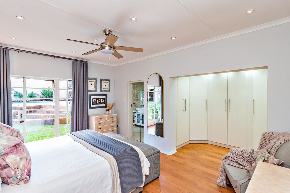 Spacious bedroom featuring built-in cupboards, laminate flooring, recessed lighting, and a ceiling fan, with direct access to the garden through sliding glass doors.