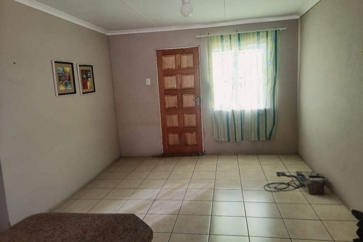 A simple living room featuring tiled flooring, a wooden panel door, and a window with security bars.