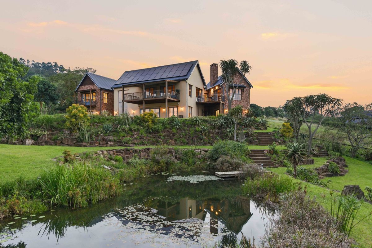 A stunning rear view of a multi-level residence featuring stone accents, timber balconies, solar panels, and a beautifully landscaped garden with a natural pond.