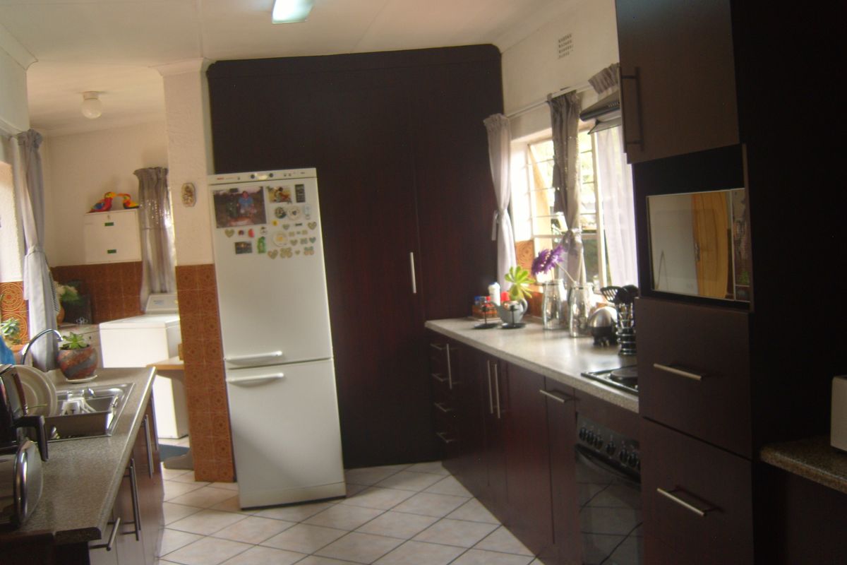 A functional kitchen featuring dark wood cabinetry, laminate countertops, built-in oven, and tiled flooring, with an adjacent laundry area visible.